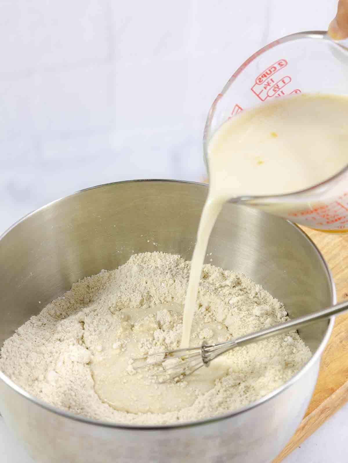 milk being poured into a mixing bowl with flour.