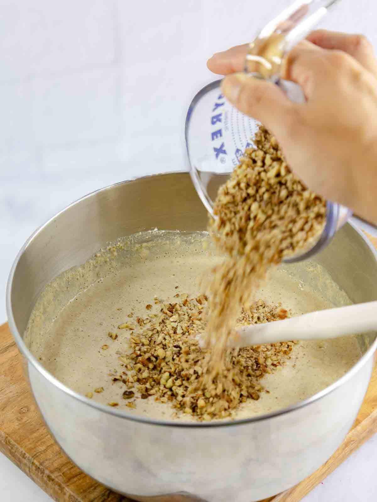 chopped pecans being poured into waffle batter.