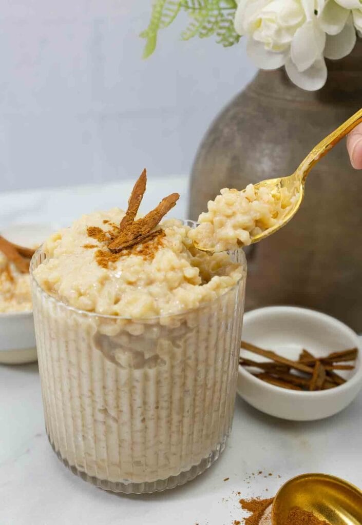 decorative glass with brown rice arroz con leche being served with a spoon.