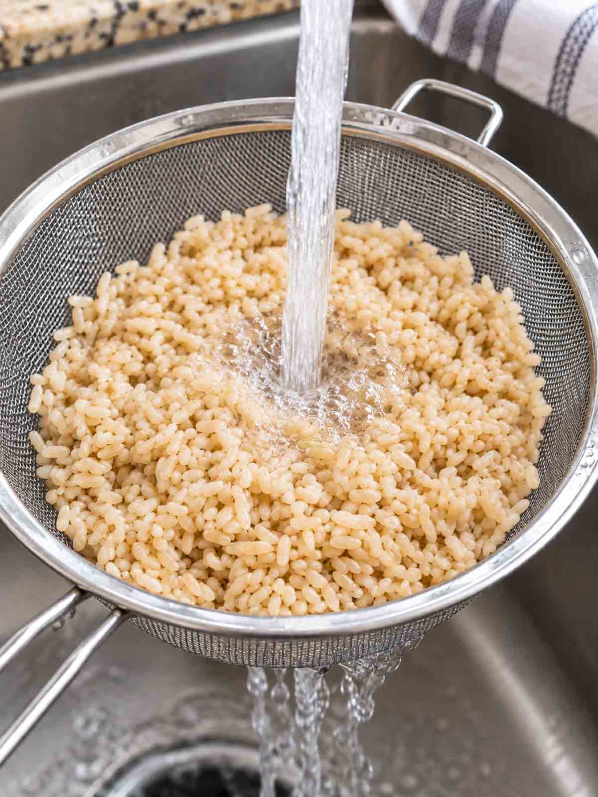 brown rice being rinsed in a mesh strainer.