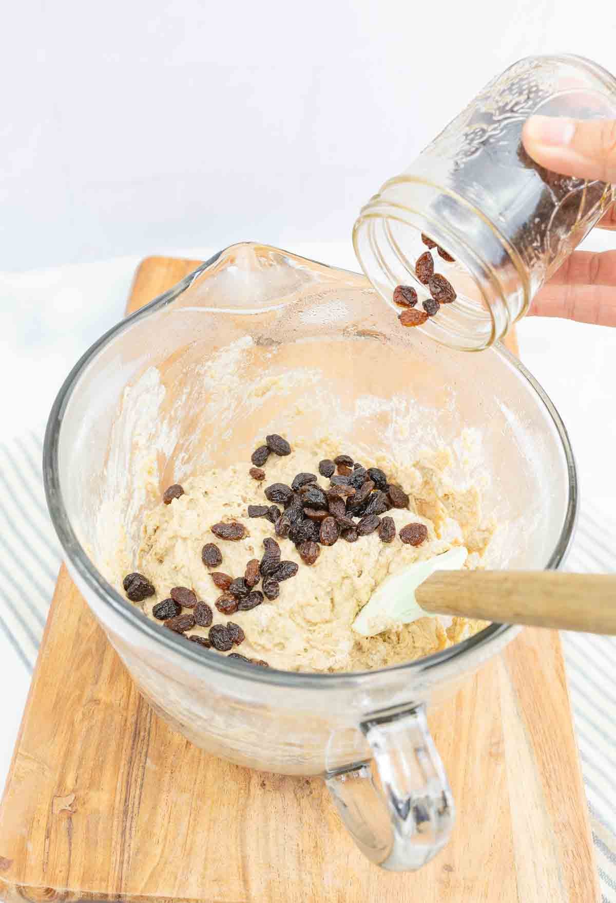 mixing bowl with cinnamon bread batter with raisins being added to dough.