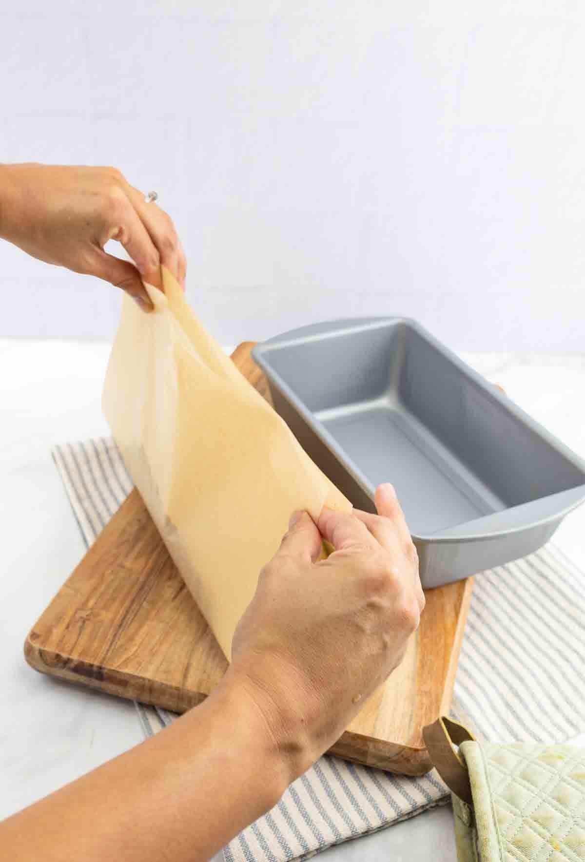 cinnamon bread dough in parchment paper being placed in a loaf pan.