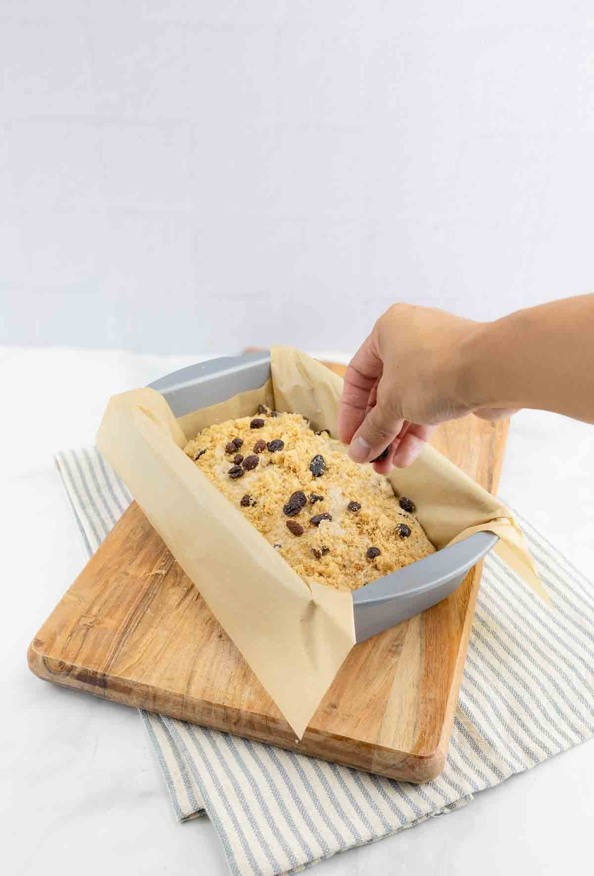 cinnamon bread being sprinkled and topped with raisins and brown sugar.