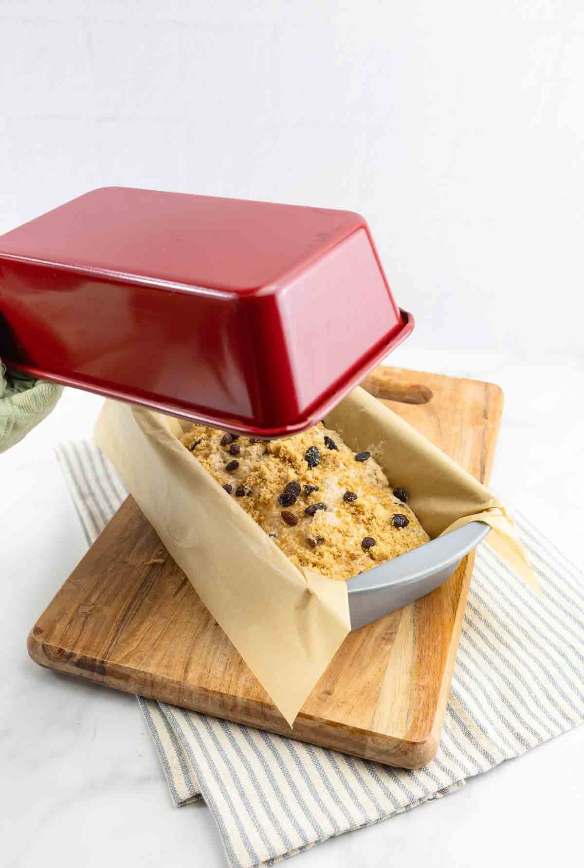 raisin bread in a loaf pan with another pan on top to create a dutch oven.