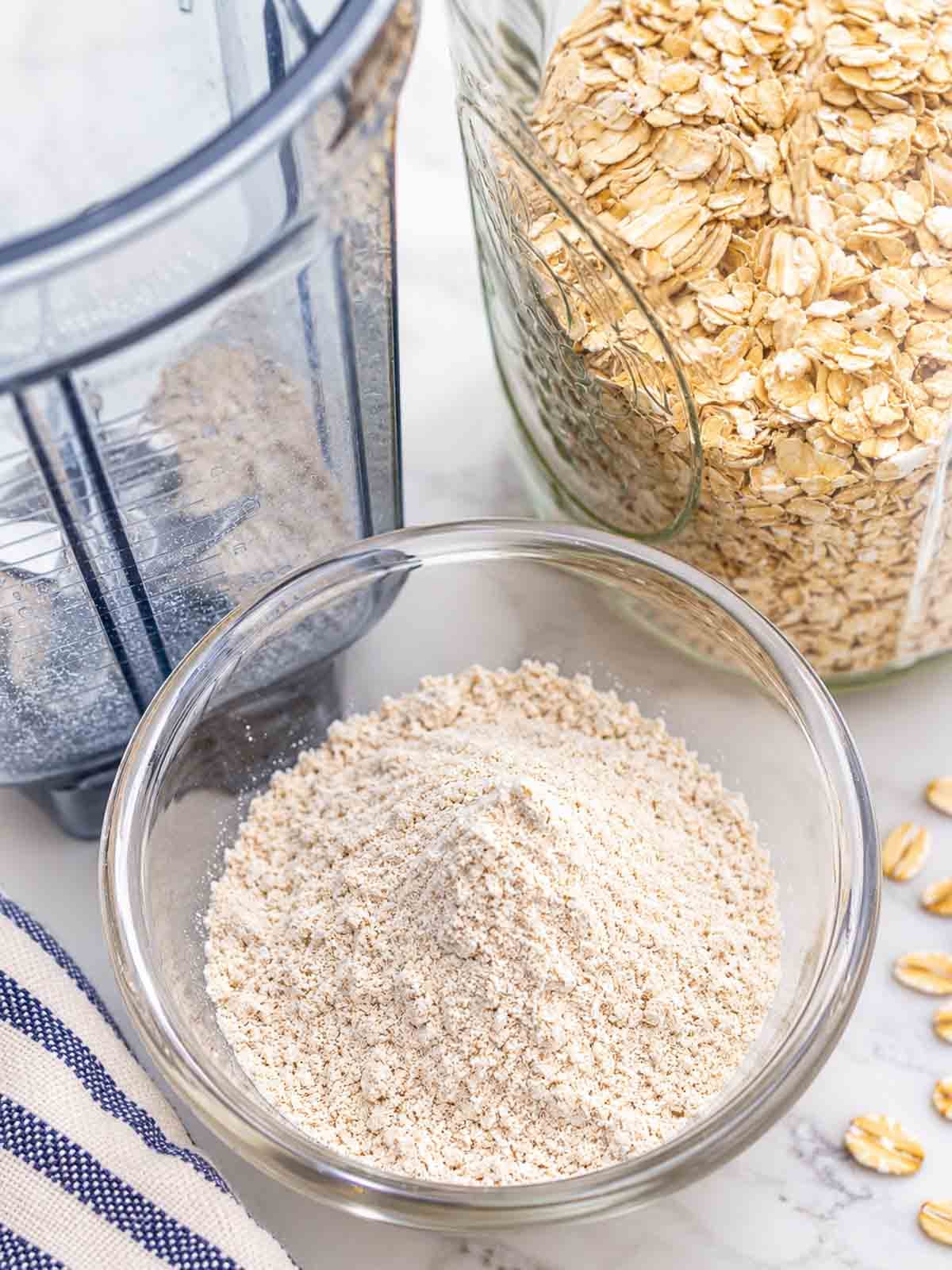 blender, jar of whole oats, and dish of oat flour showing how to make homemade oat flour.