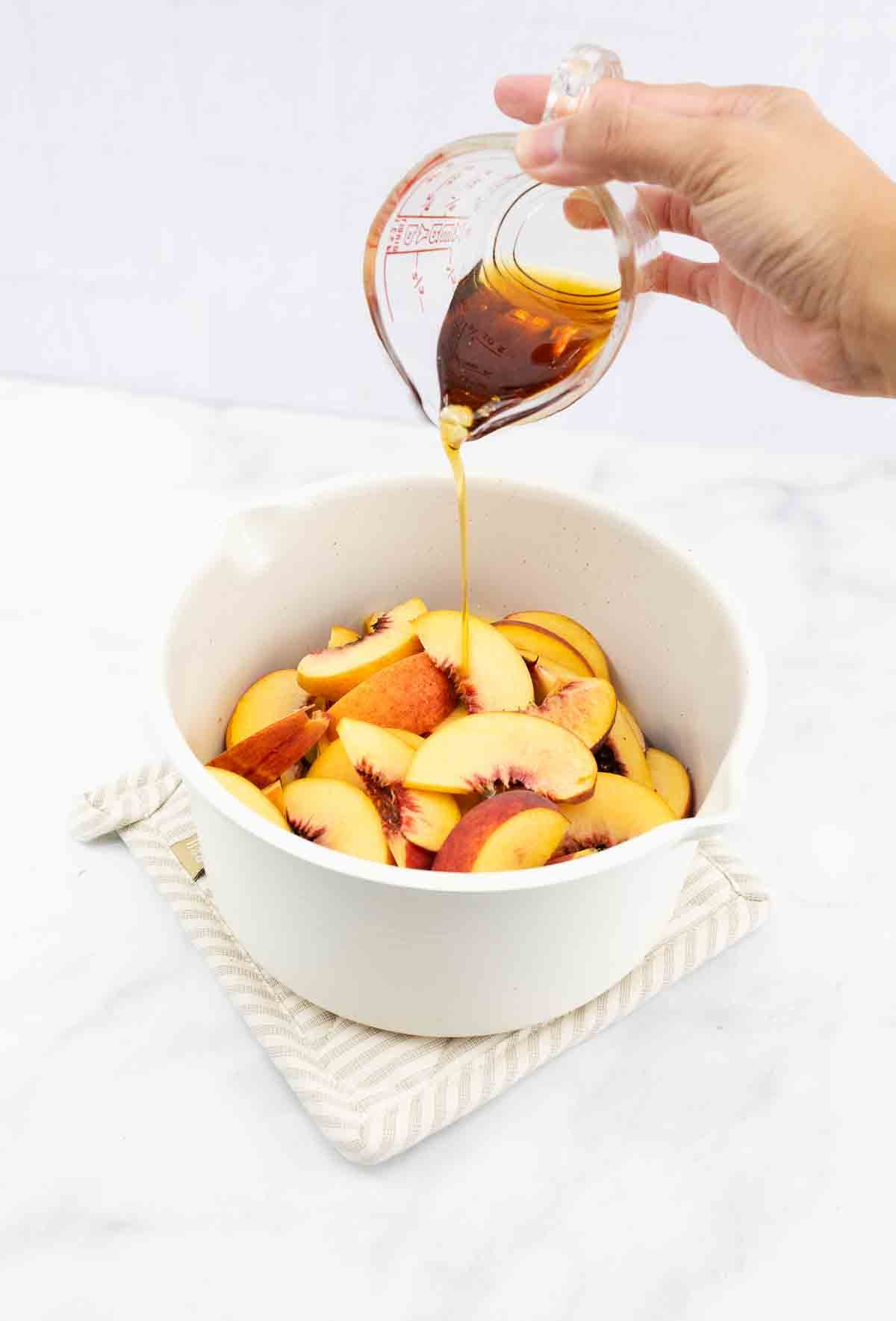 maple syrup being poured into a pan with fresh peaches.