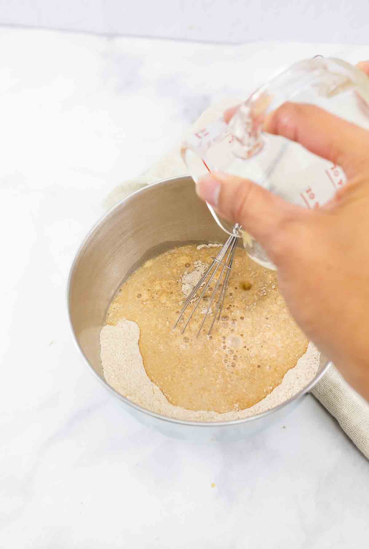 water being poured into a mixing bowl with flour and baking dry ingredients.