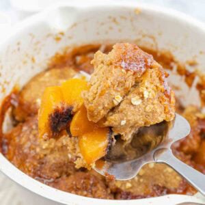 oven dish of baked peach cobbler with one slice being served.