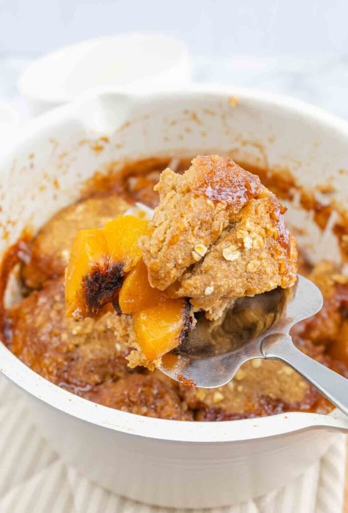 oven dish of baked peach cobbler with one slice being served.