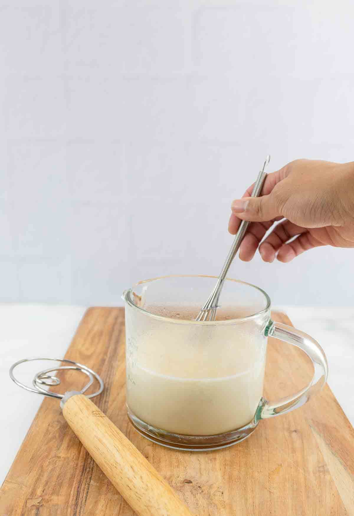 yeast being activated in liquid in a measuring cup with a whisk.